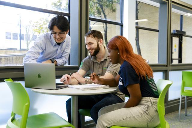Group of students gather around a table to look at a laptop
